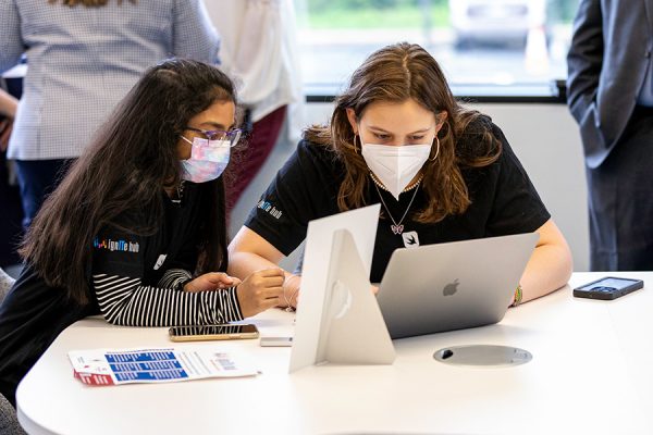 Two Female Students Working Together On A Laptop Computer At A Table In The Ignite Hub Whiles Wearing Nose Masks And A Black T-shirt.